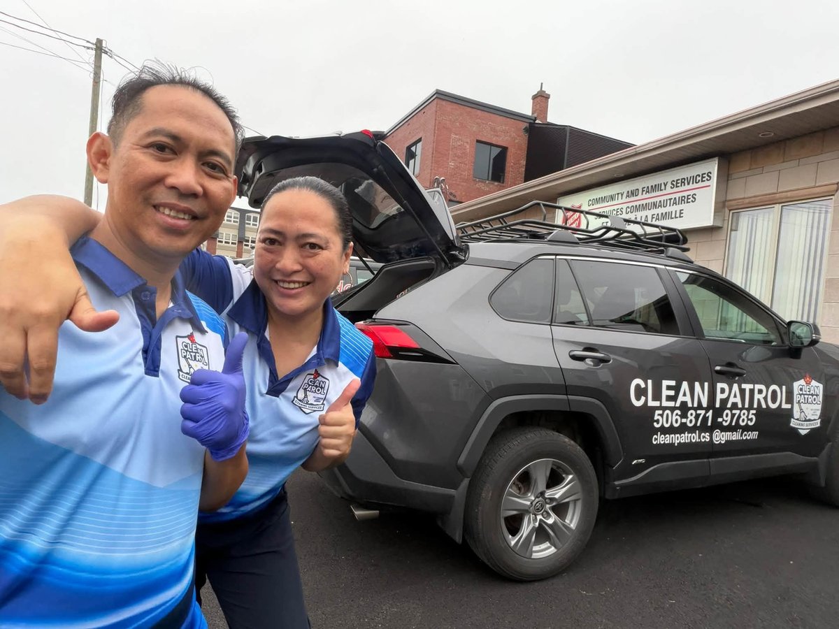Two people in blue uniforms smiling next to a black Clean Patrol vehicle with open trunk
