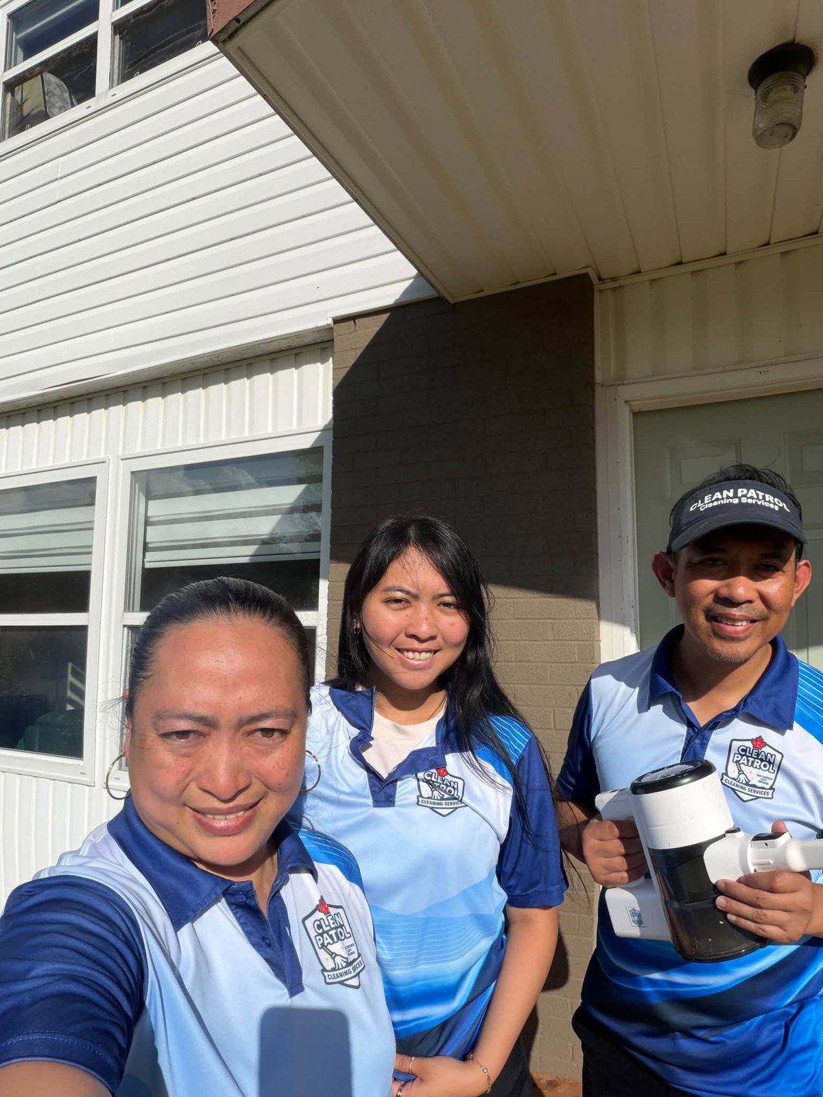 Three service workers in blue uniforms smiling at camera outside a residential home