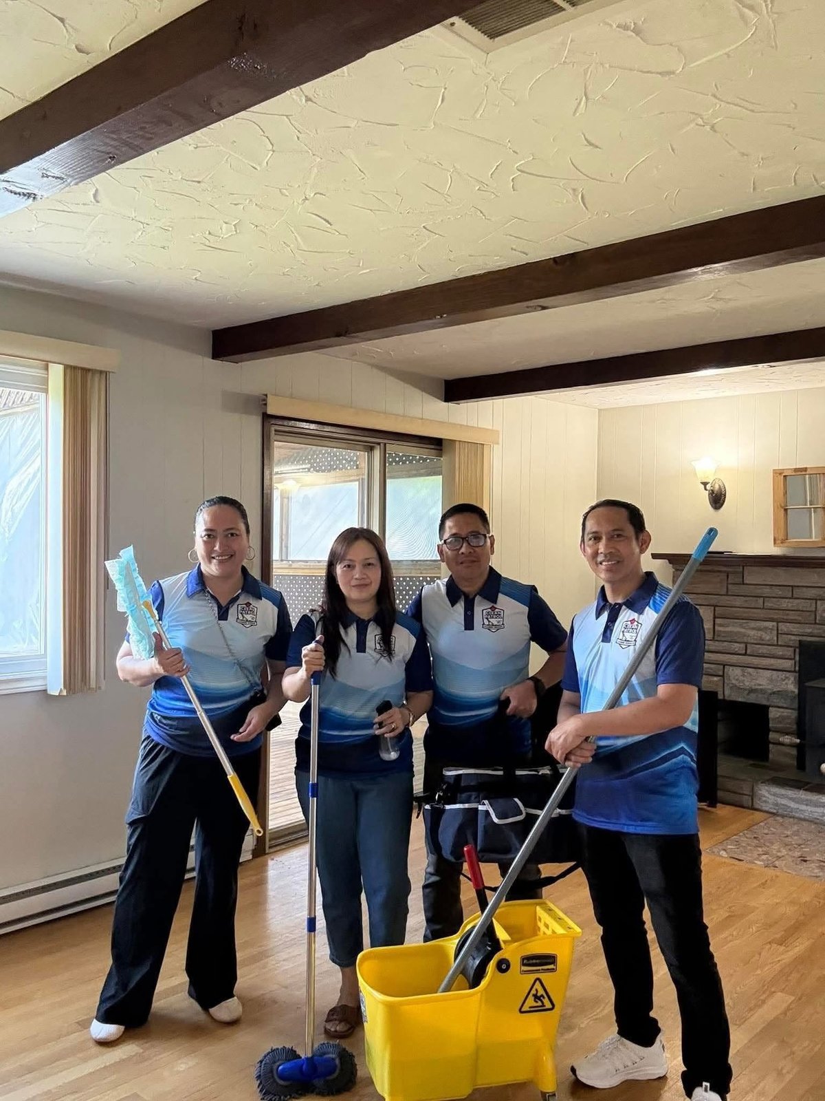 Four cleaning staff members in blue uniforms posing with mops and cleaning supplies in a residential living room